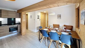 A modern kitchen with wooden cabinets, a built-in oven, and a dining area with a wooden table and blue chairs. - La Bruyère - appartement - 6pers (Les Gets)
