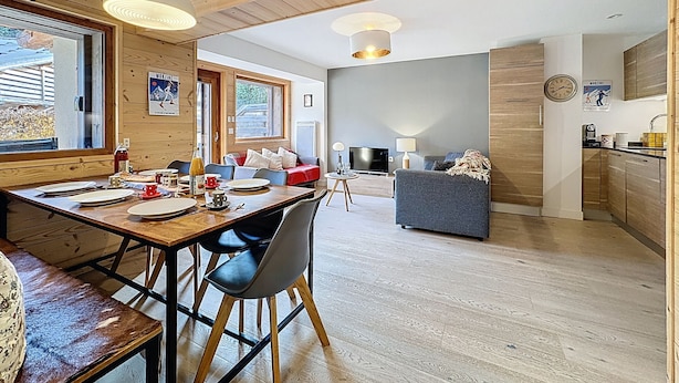 A modern living space with a wooden dining table, chairs, a sofa, and a kitchen area. - La Bruyère - appartement - 6pers (Les Gets)