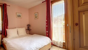 A bedroom with a bed, a nightstand, a lamp, two framed pictures, and a window with curtains. - Clos 11 - appartement - 8 pers - proche centre (Les Gets)