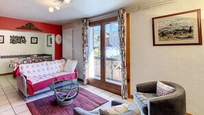 A room with a bed, a chair, a small table, a radiator, a window with curtains, and a framed picture on the wall. - Clos 11 - appartement - 8 pers - proche centre (Les Gets)