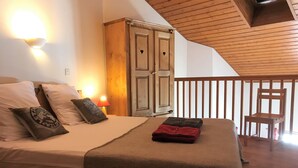 A bedroom with a bed, pillows, a nightstand with a lamp, a wardrobe, and a chair.