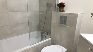 A modern bathroom with a glass-enclosed shower, a white toilet, and a small vase with flowers on the wall.