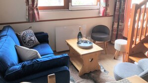 Una sala de estar acogedora con un sofá azul, una mesa de centro de madera con vasos y una botella, un sillón gris y una escalera.