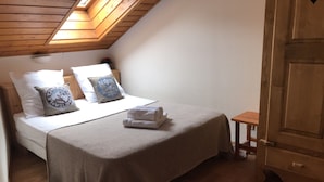 Un dormitorio con techo de madera, una cama con ropa de cama blanca, una mesita pequeña y un armario.