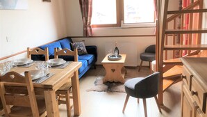 Un comedor con una mesa de madera dispuesta para cuatro, un sofá azul y una pequeña mesa auxiliar de madera con una botella y vasos.