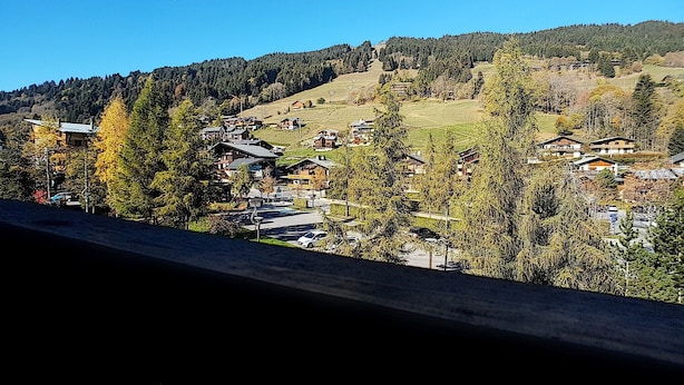 Un pueblo de montaña con casas tradicionales, cielo despejado y una ladera boscosa.