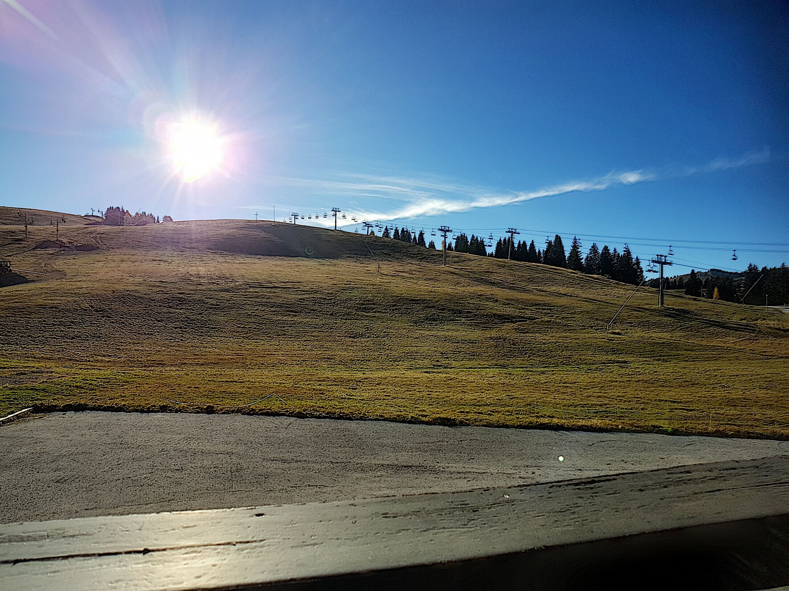 Eine hügelige Landschaft mit blauem Himmel, einer Seilbahn und einer Straße.