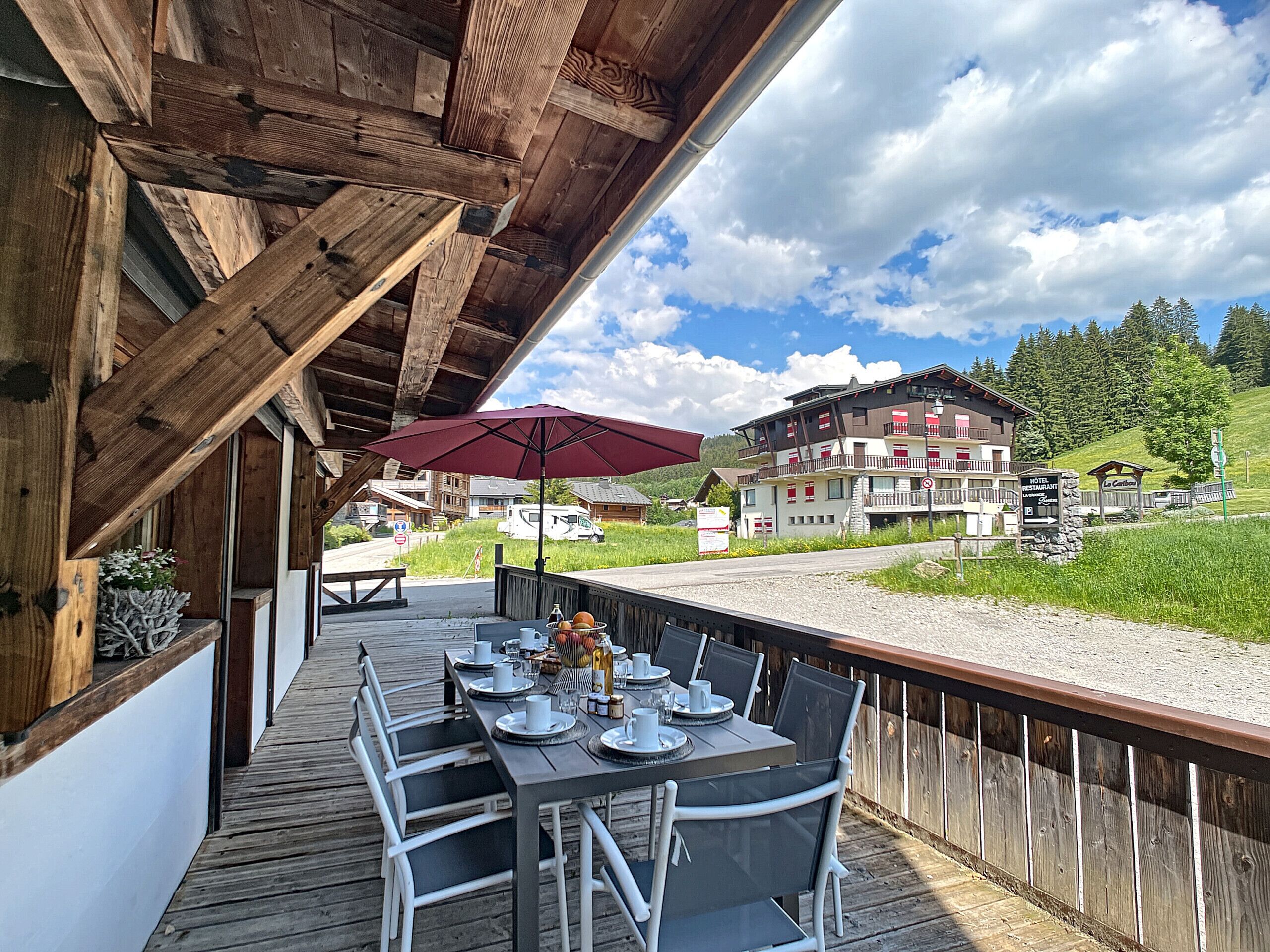 A wooden deck with a table set for dining, overlooking a mountainous area with a hotel and restaurant in the background.