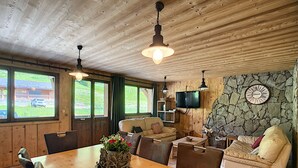 A wooden interior with a dining table, chairs, a sofa, and a television mounted on a stone wall. - Koa - appartement - 8 pers - ski-in/out (Les Gets)