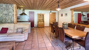 A spacious living area with a wooden ceiling, a stone wall, a kitchen with modern appliances, and a dining area with a wooden table and chairs. - Koa - appartement - 8 pers - ski-in/out (Les Gets)