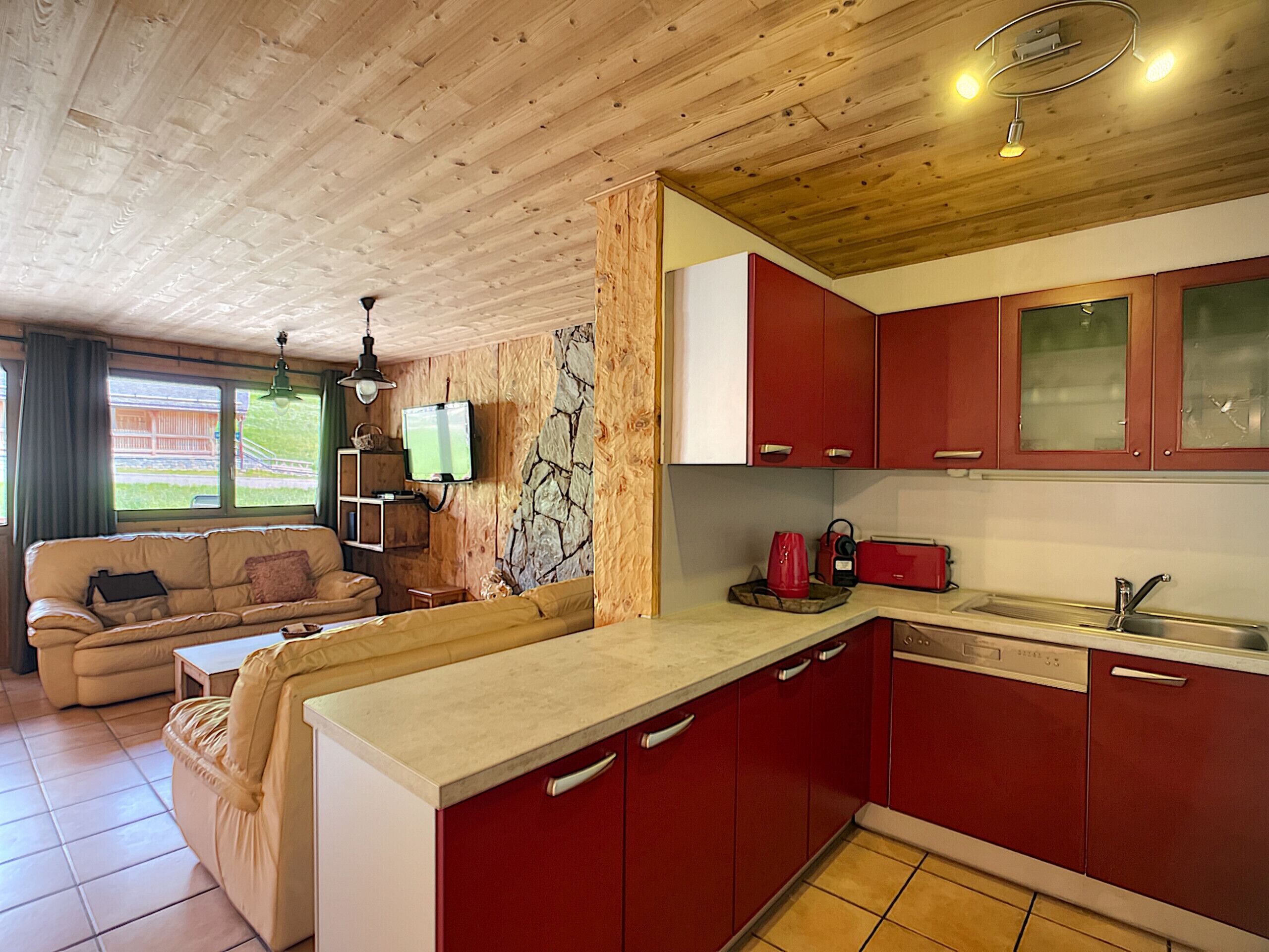A compact kitchen with red cabinets, a beige countertop, and a stone accent wall.
