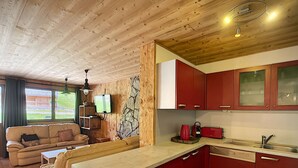 A compact kitchen with red cabinets, a beige countertop, and a stone accent wall. - Koa - appartement - 8 pers - ski-in/out (Les Gets)