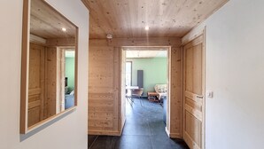 Un pasillo de madera con un espejo, una puerta que da a una habitación con cama y televisor, y un suelo de baldosas.