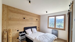 Un dormitorio con pared de madera, cama con ropa blanca, mesita de noche y ventana con vistas al exterior.