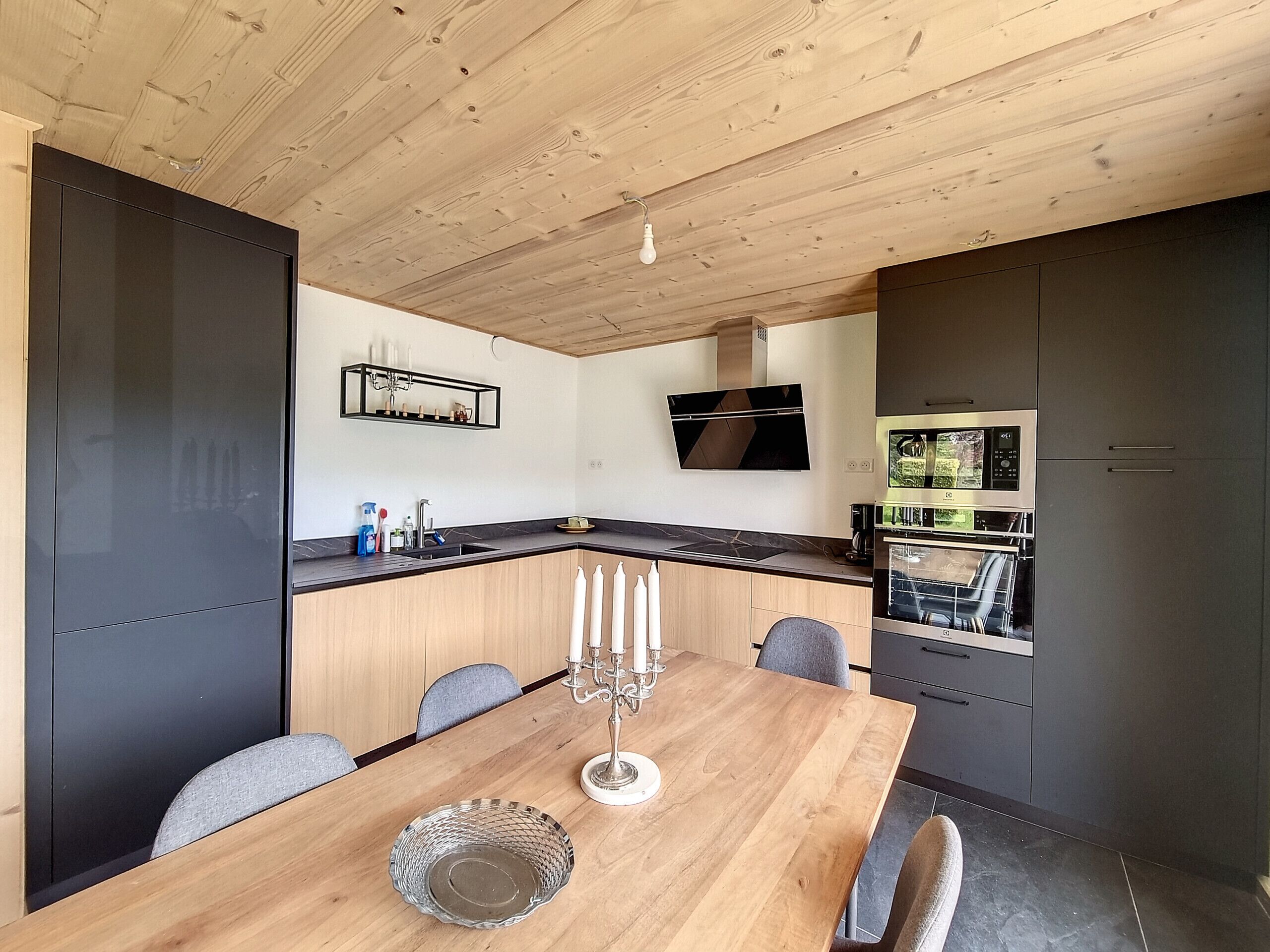 Une cuisine moderne avec un plafond en bois, un four encastré et un coin repas comprenant une table et des chaises.