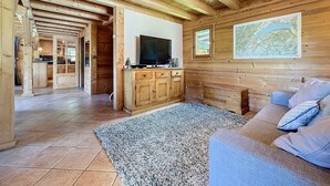 A wooden interior with a TV on a cabinet, a map on the wall, and a sofa with pillows. - Chalet Leonie - 10 pers - proche centre (Les Gets)