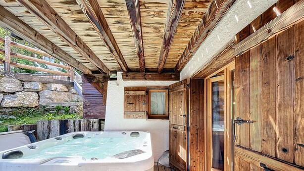 A wooden deck with a hot tub, stone wall, and wooden cabinets. - Chalet Leonie - 10 pers - proche centre (Les Gets)