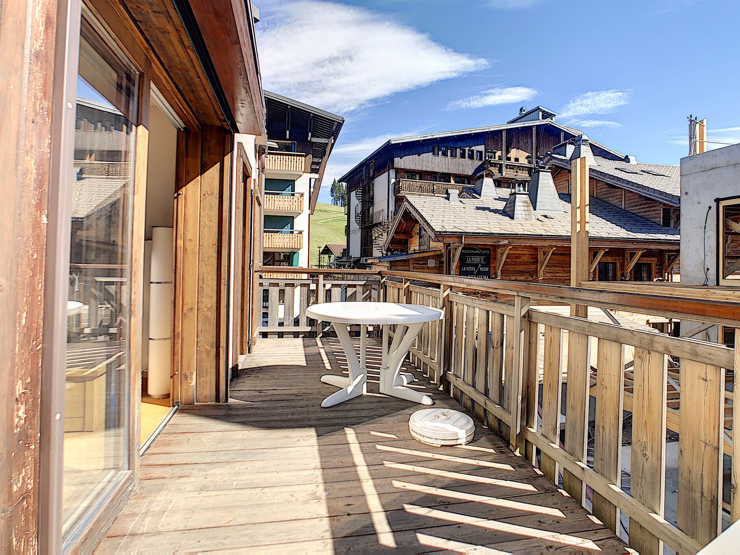 A wooden deck with a table and chairs, a view of buildings in the background, and a clear sky.
