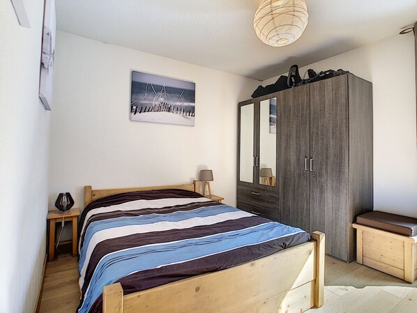 Een slaapkamer met een bed, een kledingkast, een nachtkastje en een lamp.