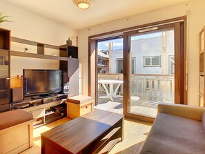 Een moderne woonkamer met een flatscreen televisie, houten meubels en een schuifdeur die leidt naar een terras.