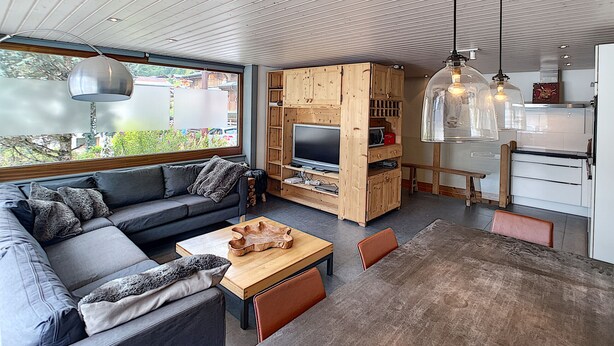Un espace de vie moderne comprenant un canapé, une table basse, un téléviseur, un meuble de rangement en bois et un coin cuisine.