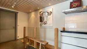 Une cuisine moderne avec un banc en bois, un tableau représentant une vache et une hotte aspirante en acier inoxydable.