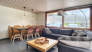 Un intérieur moderne comprenant un coin repas, un canapé et une grande fenêtre donnant sur les voitures garées.