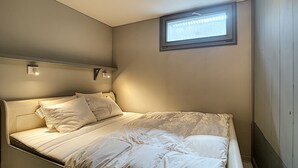 Un lit simple avec une tête de lit, une petite fenêtre et deux appliques murales.