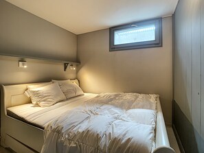 Un lit simple avec une tête de lit, une petite fenêtre et deux appliques murales.