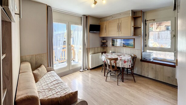 A cozy room with a sofa, a dining table with chairs, a TV, wooden cabinets, and a window with curtains. - Ceylan - appartement - 5 pers - centre (Les Gets)