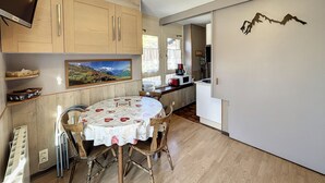 A compact kitchen with wooden cabinets, a dining table with chairs, a mounted TV, and a scenic painting. - Ceylan - appartement - 5 pers - centre (Les Gets)