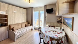 A compact living space with a sofa, a dining table, a TV, and built-in wooden shelving. - Ceylan - appartement - 5 pers - centre (Les Gets)