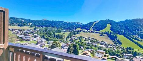 Vista panorámica desde un balcón con vistas a un pueblo, casas y colinas verdes.
