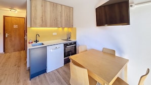 A compact kitchen with wooden cabinets, a dishwasher, a sink, and a dining table with chairs.