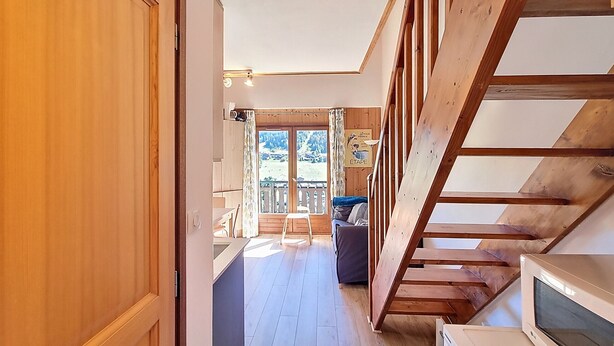 A wooden interior with a staircase, a kitchen area, and a balcony with a view of the outdoors.