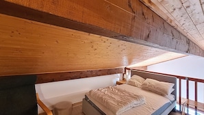 A wooden ceiling with exposed beams, a bed with a mattress and pillows, and a small bedside table.