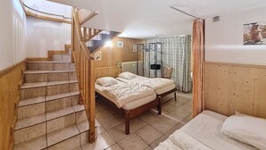 Une chambre avec un escalier en bois, deux lits, un radiateur et un espace douche.