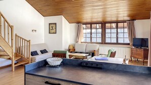A modern kitchen with a wooden ceiling, a dining area with a table and chairs, a television, and a window with curtains. - Cornuts 3 - appartement - 7pers (Les Gets)
