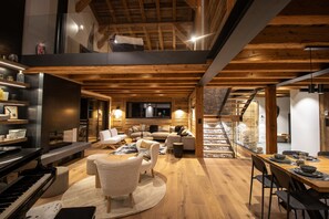 A modern interior with a wooden ceiling, a piano, sofas, a dining area, and a staircase. - Chalet Caly - 15pers - vue montagne (Les Gets)