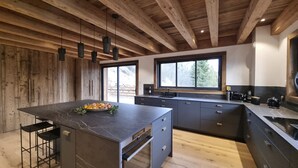 A modern kitchen with a large island, dark cabinetry, and a wooden ceiling. - Chalet Caly - 15pers - vue montagne (Les Gets)