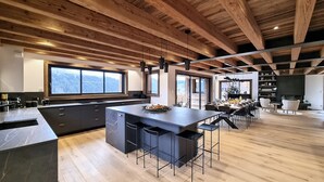 A modern kitchen with a large island, wooden beams, and a view of the outdoors. - Chalet Caly - 15pers - vue montagne (Les Gets)