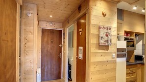 A wooden interior with a kitchen area, including a refrigerator, oven, and wooden cabinets. - Edelweiss- appartement - 7pers -proche centre (Les Gets)
