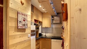 A compact kitchen with wooden cabinetry, a built-in oven, and a dishwasher. - Edelweiss- appartement - 7pers -proche centre (Les Gets)