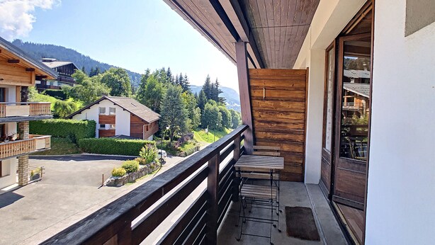 A balcony with a wooden railing overlooking a residential area with houses and greenery. - Edelweiss- appartement - 7pers -proche centre (Les Gets)