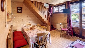 A cozy dining area with a wooden staircase, a table with a floral tablecloth, and a bench with red cushions. - Edelweiss- appartement - 7pers -proche centre (Les Gets)