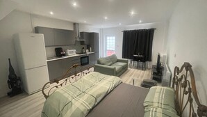 Ein kompakter Wohnraum mit Küchenzeile, einem Bett mit grüner Bettwäsche, einer Couch und einem Essbereich.