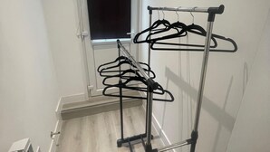Ein Zimmer mit einem Wäscheständer aus Metall an der Wand, einem Fenster mit Rollläden und einer Fußbodenheizung.