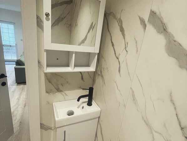 Une salle de bain avec un pare-baignoire en marbre, un lavabo blanc avec un robinet noir et un miroir au-dessus du lavabo.