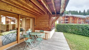 Una cabaña de madera con terraza, mobiliario exterior y vistas a un área boscosa.