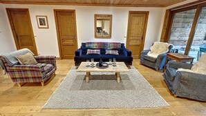 Una sala de estar acogedora con un sofá azul, sillones a cuadros, una mesa de centro y puertas de madera.